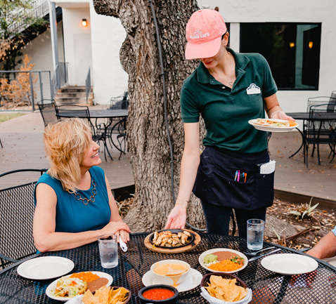 A server bringing plates to guests on the patio